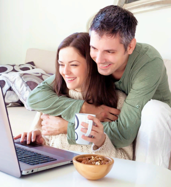 Счастливая семейная пара за ноутбуком. Женщина держит кружку, рядом на столе стоит тарелка с орехами